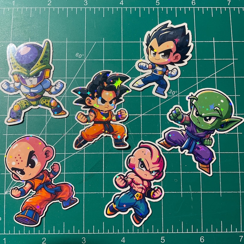 May include: A collection of seven colorful stickers featuring characters from the Dragon Ball anime series. The stickers depict various characters in dynamic action poses, with vibrant colors and holographic accents. The background is a green cutting mat.