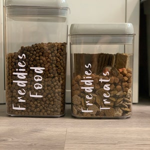 May include: Two clear plastic containers with grey lids, filled with pet food and treats. The containers are labelled "Freddies Food" and "Freddies Treats".