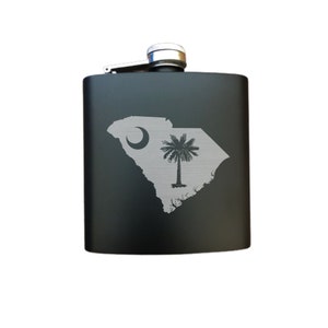 May include: Black stainless steel flask with a silver cap and an engraved design of the state of South Carolina with the state flag.
