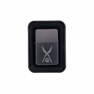 May include: A black lighter with a silver finish and a design of two crossed swords and a paw print.