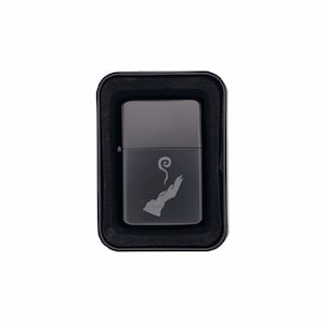 May include: A black metal lighter with a silver hand and smoke design. The lighter is in a black box.