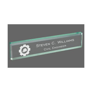May include: A clear green glass desk nameplate with a white gear and hard hat icon. The nameplate reads "STEVEN C. WILLIAMS CIVIL ENGINEER".