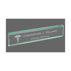 May include: A clear green glass desk nameplate with a white engraved medical symbol and the text "Christopher J. Williams, Internal Medicine".