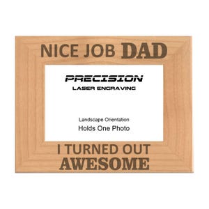 May include: A light wood picture frame with the text "NICE JOB DAD" and "I TURNED OUT AWESOME" engraved on it. The frame is for a landscape-oriented photo and has the words "PRECISION LASER ENGRAVING" printed on it.