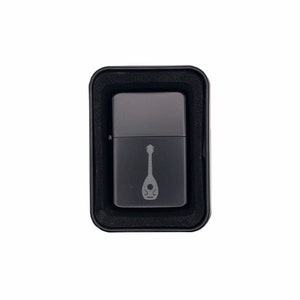 May include: A black lighter with a silver finish and a mandolin design engraved on the front. The lighter is in a black box.