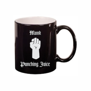 May include: Black ceramic mug with a white interior and a large handle. The mug features the text "Monk" above a white fist graphic, and the words "Punching Juice" below the graphic, all in a gothic font.