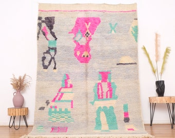 May include: A vintage Moroccan rug with a light blue background and colorful geometric patterns in pink, green, and black. The rug has a fringe border and is made of wool.