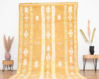 May include: A large, rectangular, handwoven rug with a geometric pattern in shades of yellow and white. The rug has a fringe border and is made of wool.