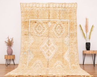 May include: A large, cream-colored Moroccan rug with a white geometric pattern. The rug has a fringe border and is made of wool.