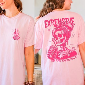 May include: Pink t-shirt with a graphic of a skeleton wearing a crown and holding a drink. The text "Expensive, Difficult, and Talks Back" is printed below the graphic.
