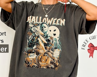 May include: A dark gray t-shirt with a graphic print of a horror movie character holding a knife and standing in front of pumpkins. The text "HALLOWEEN" is printed above the character.
