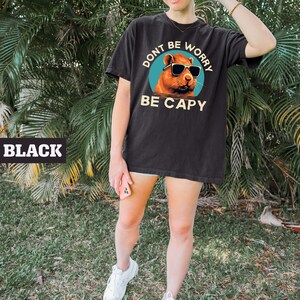 May include: Black t-shirt with a graphic of a capybara wearing sunglasses and the text "Don't be worry be capy".