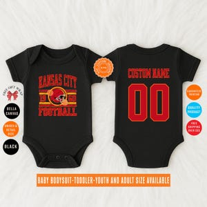 May include: Black baby bodysuit with a red and gold "Kansas City Football" design on the front. The back features a red "00" with a red outline and the text "CUSTOM NAME". The bodysuit is available in baby, toddler, youth, and adult sizes.