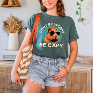 May include: A teal green t-shirt with a graphic of a capybara wearing sunglasses and the text "Don't be worry be capy".