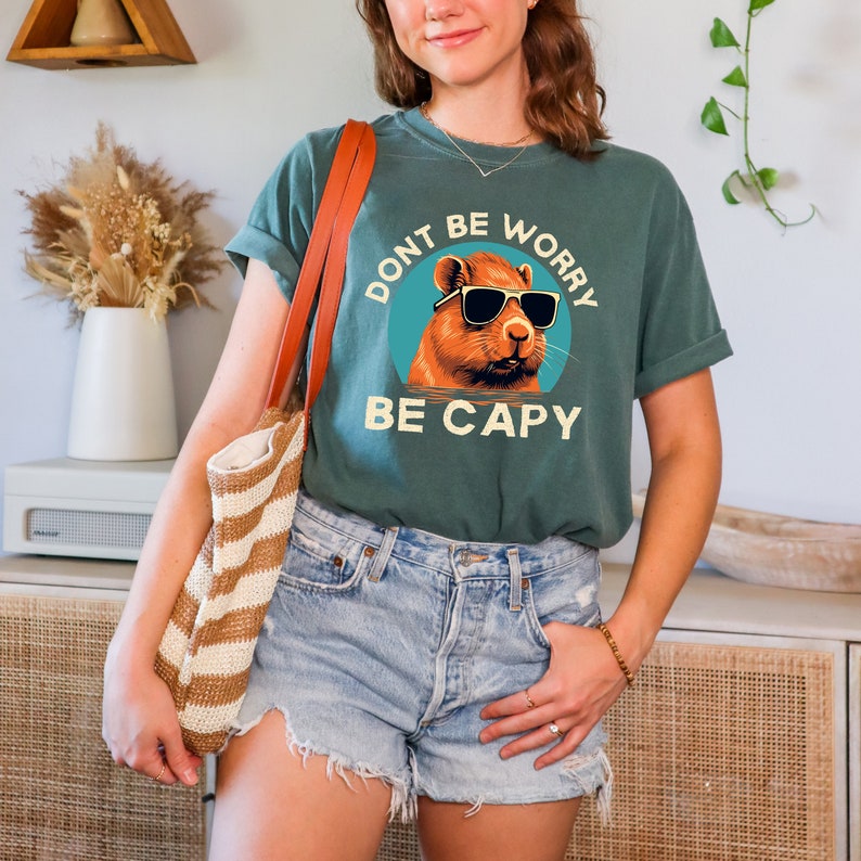 May include: A teal green t-shirt with a graphic of a capybara wearing sunglasses and the text "Don't be worry be capy".
