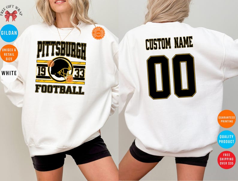 May include: White sweatshirt with a Pittsburgh Steelers football design. The front features the team name, helmet graphic, and the years 1933. The back has the option for a custom name and the number 00 in black and gold.