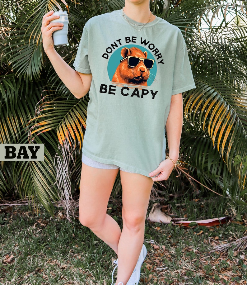 May include: A light green t-shirt with a graphic of a capybara wearing sunglasses and the text "Don't be worry be capy".