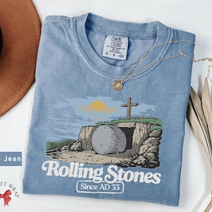 May include: A blue t-shirt with a graphic of a stone tomb with a cross and the text "Rolling Stones Since AD 33".