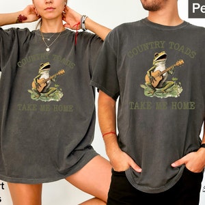 May include: A dark gray t-shirt with a graphic of a frog playing a guitar. The text "COUNTRY TOADS TAKE ME HOME" is printed on the shirt.