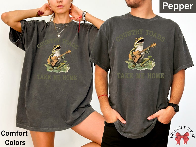 May include: A dark gray t-shirt with a graphic of a frog playing a guitar. The text "COUNTRY TOADS TAKE ME HOME" is printed on the shirt.