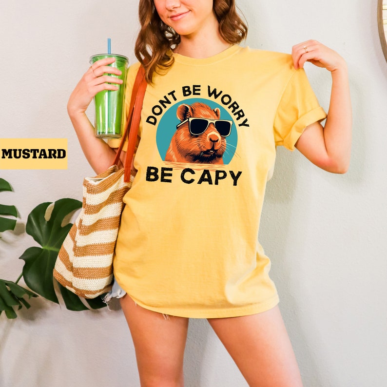 May include: Yellow t-shirt with a graphic of a capybara wearing sunglasses and the text "Don't be worry be capy".