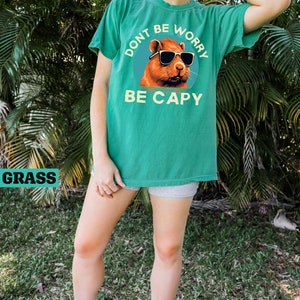 May include: A green t-shirt with a graphic of a capybara wearing sunglasses. The text on the shirt reads "Don't be worry, be capy".
