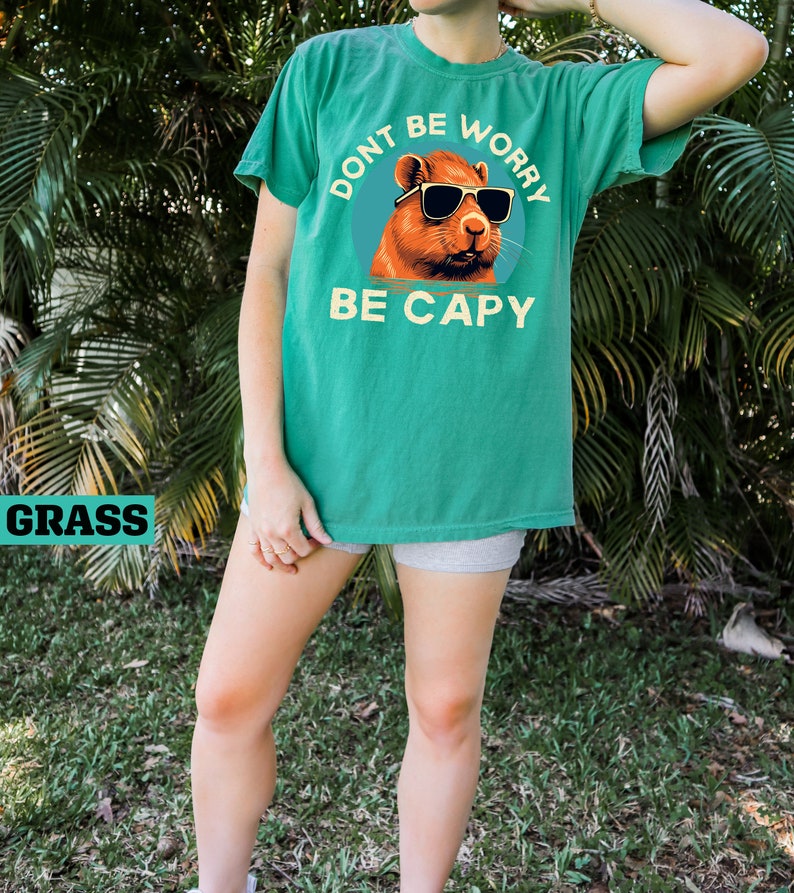 May include: A green t-shirt with a graphic of a capybara wearing sunglasses. The text on the shirt reads "Don't be worry, be capy".