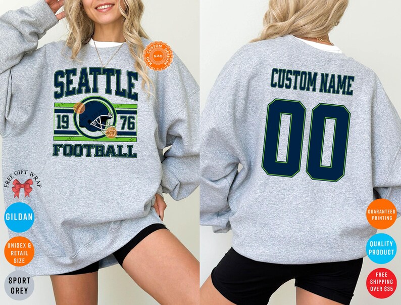 May include: Sport grey sweatshirt with "SEATTLE FOOTBALL 1976" graphic on the front. The design includes a football helmet in navy blue and green. The back of the sweatshirt has "CUSTOM NAME" and the number "00" in navy blue.
