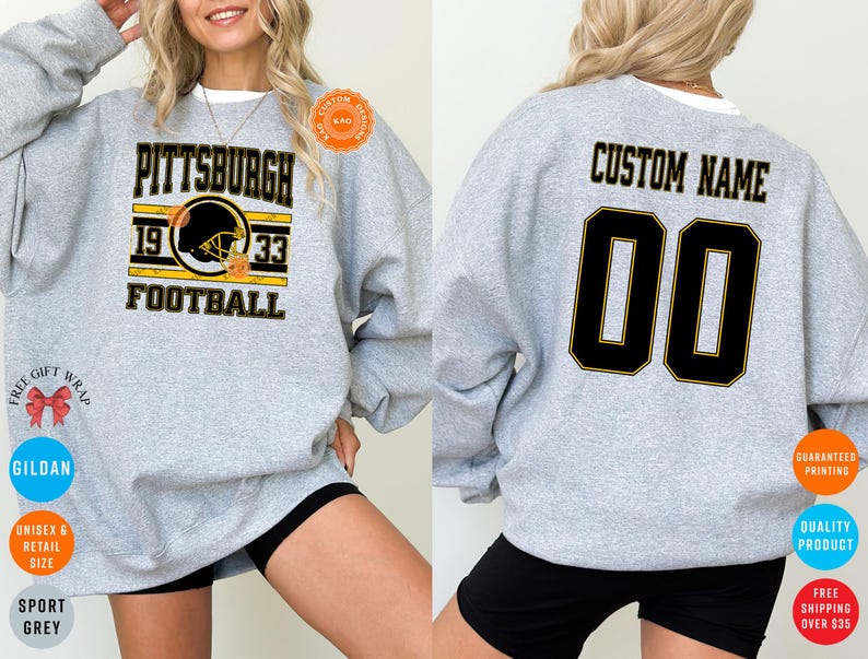 May include: A light gray sweatshirt with the word "PITTSBURGH" in black and gold lettering, along with "1933 FOOTBALL" and a football helmet graphic. The back of the sweatshirt has "CUSTOM NAME" and the number "00" in black and gold.