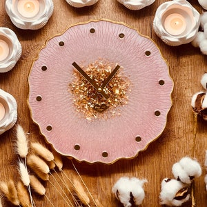 May include: A pink resin clock with gold accents and a white heart charm. The clock is surrounded by white decorative items and cotton balls.