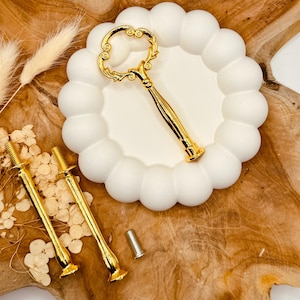Può includere: Connettore per supporto per torte dorato con un design a chiave decorativo. Il connettore ha un'estremità filettata per il fissaggio a un supporto per torte. Sono inclusi anche tre viti dorate.