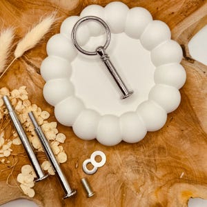 Könnte beinhalten: Ein weißer Kuchenständer mit einem gewellten Rand und einem silbernen Metallgriff. Der Ständer wird mit drei silbernen Metallstangen und zwei silbernen Metallunterlegscheiben geliefert.