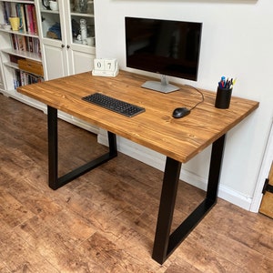 May include: A wooden desk with black metal legs. The desk has a light brown wood top and is decorated with a keyboard, mouse, and a pencil holder with coloured pencils. The desk is in a room with white walls and a white bookcase in the background.