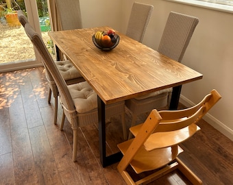 May include: A wooden dining table with black metal legs, surrounded by wicker chairs and a high chair. A bowl of fruit sits in the center of the table.