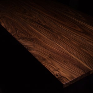 Puede incluir: Un tablero de mesa rectangular de madera con un acabado rico en color marr&oacute;n oscuro y patrones de veta pronunciados y arremolinados. La superficie muestra tonos profundos de chocolate y espresso con texturas de madera natural visibles.