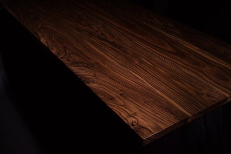 Puede incluir: Un tablero de mesa rectangular de madera con un acabado rico en color marr&oacute;n oscuro y patrones de veta pronunciados y arremolinados. La superficie muestra tonos profundos de chocolate y espresso con texturas de madera natural visibles.