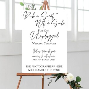May include: A white sign on a wooden easel with black script. The sign reads "Pick a Seat Not a Side For Our Unplugged Wedding Ceremony." Additional text requests guests turn off cameras and cell phones. Floral accents are visible.