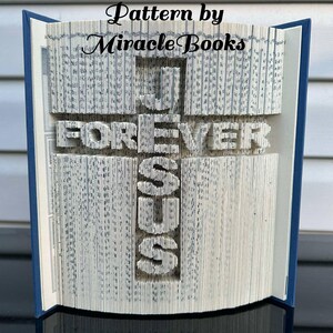 Puede incluir: Un libro doblado en forma de cruz con las palabras "JESUS" y "FOREVER" escritas en él. El libro es azul y blanco y las palabras son negras. Las palabras "Pattern by Miracle Books" están escritas en la parte superior de la imagen.