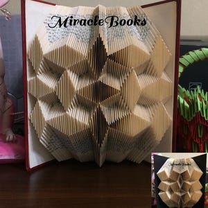 Peut inclure: Une sculpture en livre plié avec un motif géométrique en losange créé à partir de pages individuelles. Le livre a une couverture rouge foncé et présente le texte Miracle Books imprimé en noir au centre supérieur des pages en papier pliées.