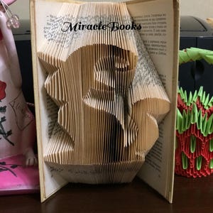 May include: A book sculpture featuring folded pages that form the shape of a squirrel. The text Miracle Books is printed across the top centre of the pages. The book is open, displaying the intricate paper folding technique used to create the design.