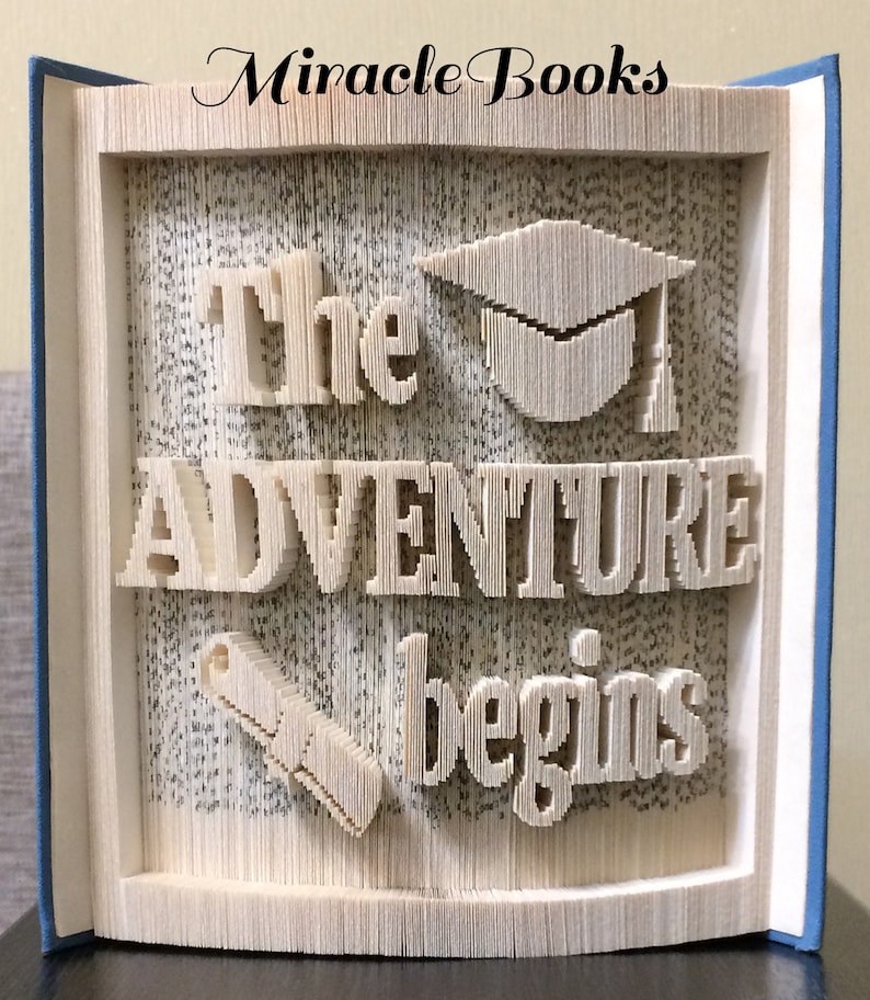 May include: A book art sculpture with the words "The Adventure Begins" and a graduation cap and a scroll made from folded book pages.