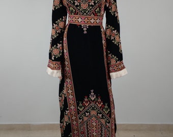 Puede incluir: Un vestido largo negro con bordados intrincados en tonos de rosa, rojo, verde y dorado. El vestido tiene un escote redondo y mangas largas con un patrón floral. El bordado presenta diseños geométricos y motivos florales.