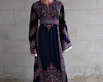 May include: A long, navy blue dress with intricate embroidery in shades of pink, blue, and gold. The dress features long sleeves and a detailed pattern around the neckline, waist, and sleeves. The dress is displayed on a mannequin.