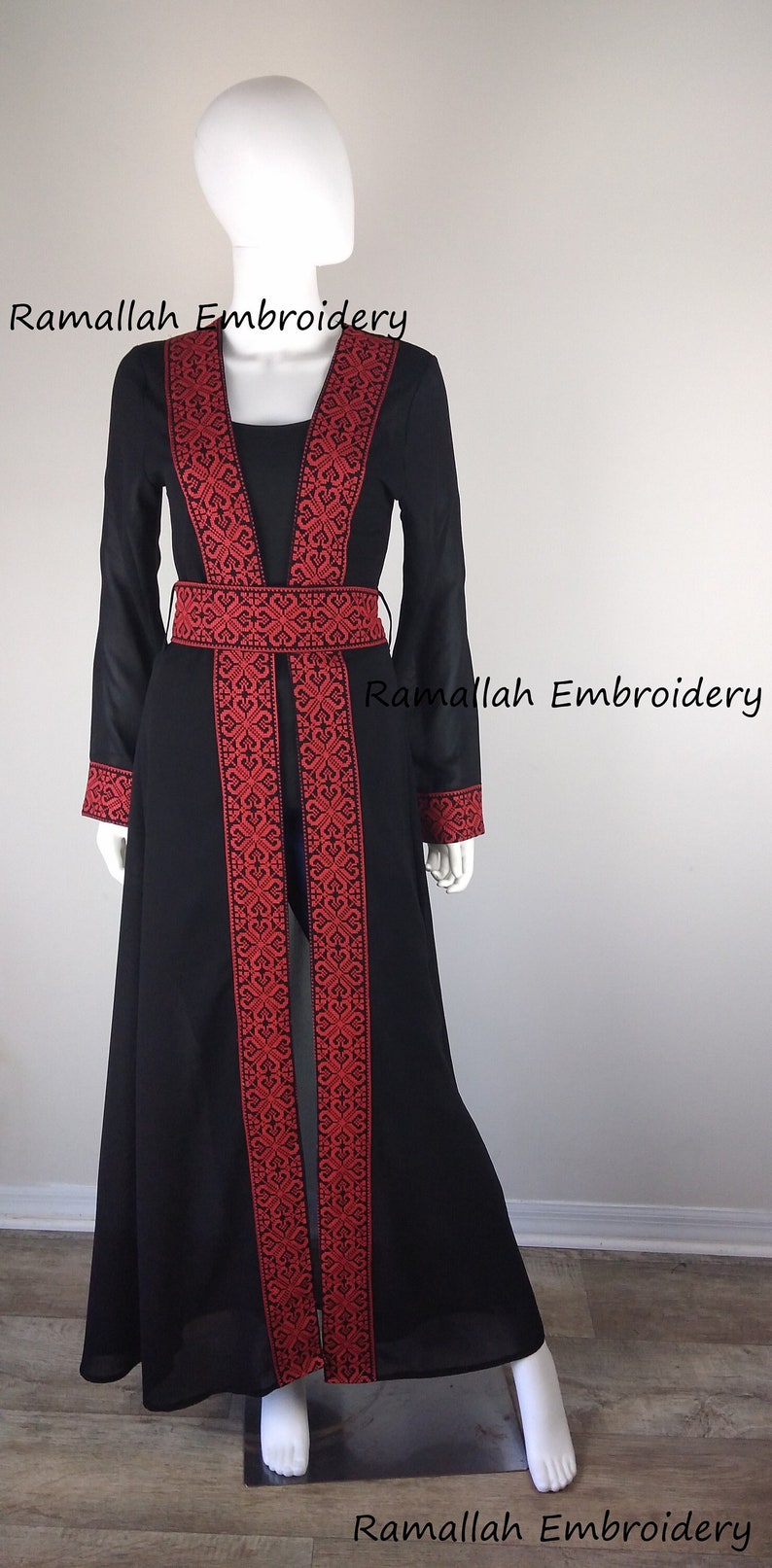 Puede incluir: Una larga abaya negra con bordados rojos. La abaya tiene un escote en V y un cintur&oacute;n. El bordado es un dise&ntilde;o tradicional palestino. El texto "Ramallah Embroidery" aparece tres veces en la imagen.