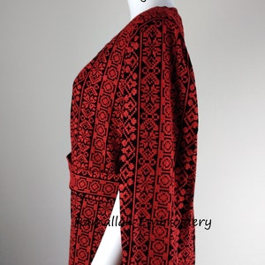 May include: A red and black embroidered dress with a V-neckline and long sleeves. The dress has a geometric pattern and is made of a soft, flowing fabric. The dress is on a white mannequin. The text "Ramallah Embroidery" is visible at the top of the image.
