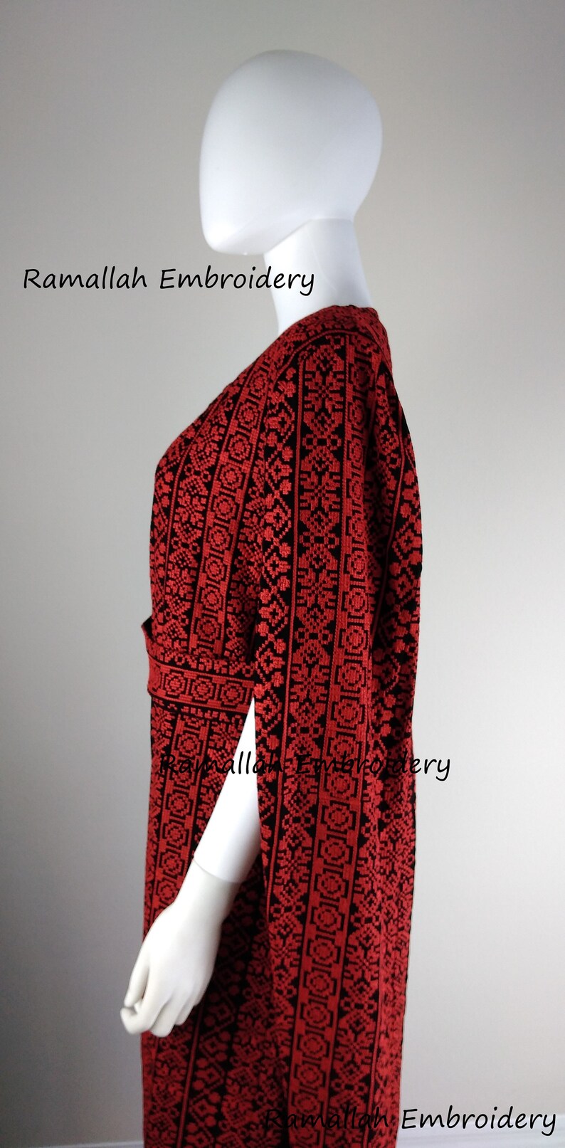 May include: A red and black embroidered dress with a V-neckline and long sleeves. The dress has a geometric pattern and is made of a soft, flowing fabric. The dress is on a white mannequin. The text "Ramallah Embroidery" is visible at the top of the image.