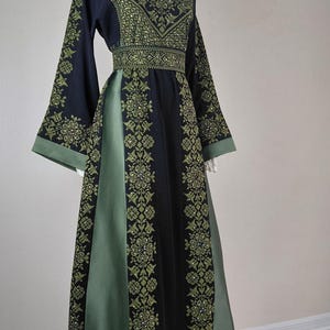 Puede incluir: Un vestido largo hasta el suelo con un diseño en negro y verde oliva con intrincados patrones geométricos bordados. La prenda incluye mangas largas y anchas, un panel de cintura ajustado y un escote en V, acentuado con pequeños detalles reflectantes.
