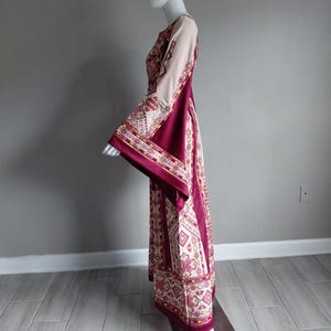 May include: A long, flowing dress with a cream-colored bodice and sleeves, and a deep burgundy skirt. The dress features intricate geometric patterns in shades of cream, burgundy, and gold. The sleeves are wide and flared, adding a dramatic flair to the garment.