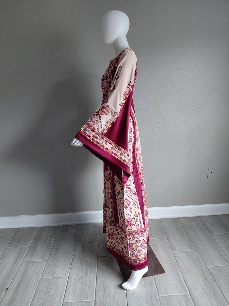 May include: A long, flowing dress with a cream-colored bodice and sleeves, and a deep burgundy skirt. The dress features intricate geometric patterns in shades of cream, burgundy, and gold. The sleeves are wide and flared, adding a dramatic flair to the garment.