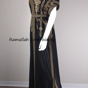 May include: Black maxi dress with gold embroidery. The dress features a V-neck, short sleeves, and a slit on the side. The dress is displayed on a mannequin. The text "Ramallah Embroidery" is visible.